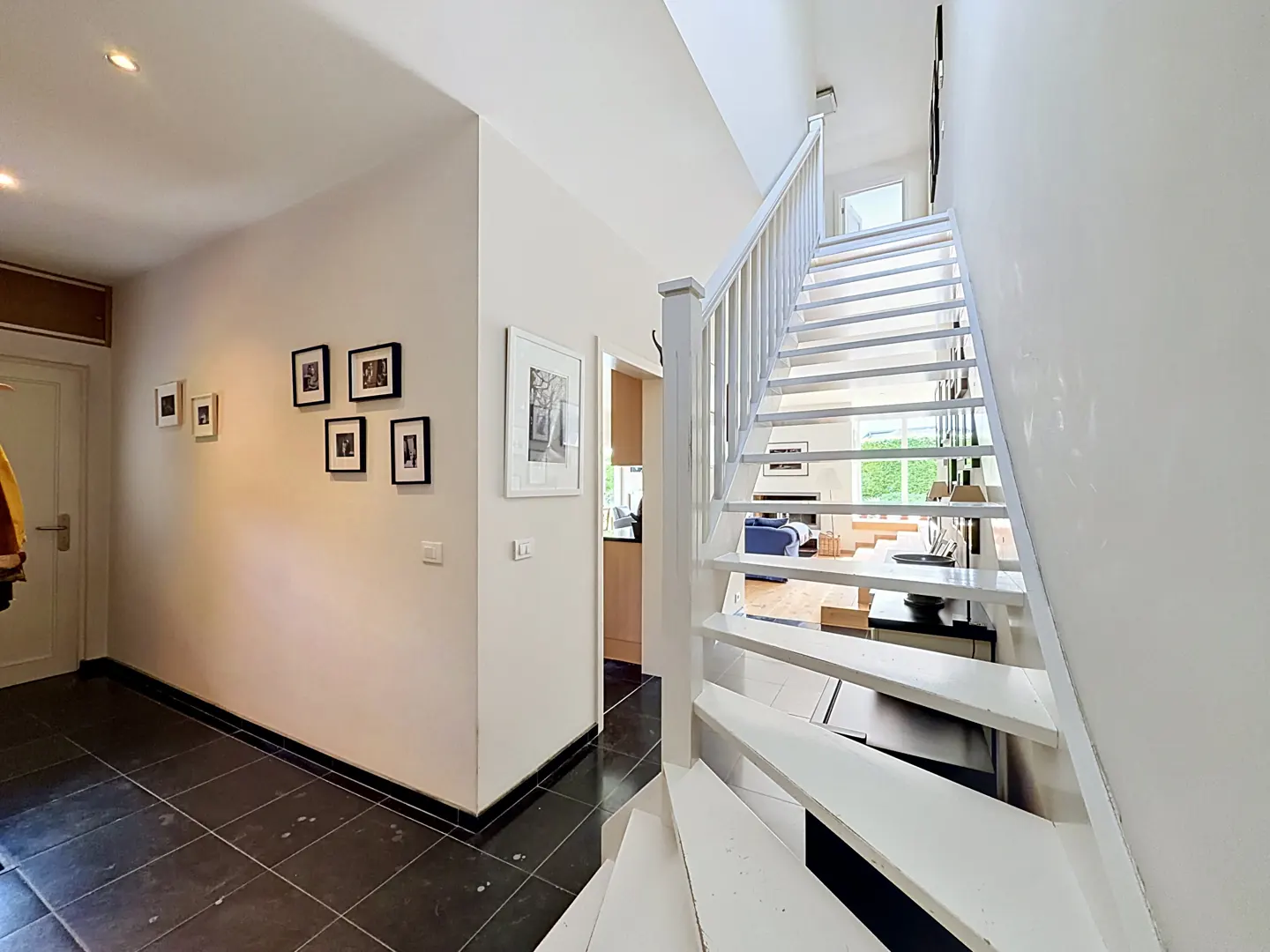 Interior view of a home featuring a white staircase, black tile floor, and framed pictures on a white wall.