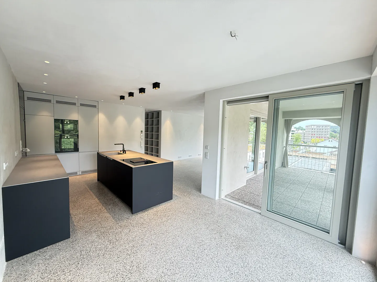 A modern, open-concept kitchen with a black island, light gray cabinets, and sliding glass doors to a balcony.