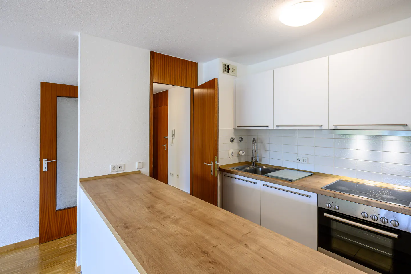 Bright kitchen with white cabinets, stainless steel appliances, and a wood countertop. A door is visible on the left.