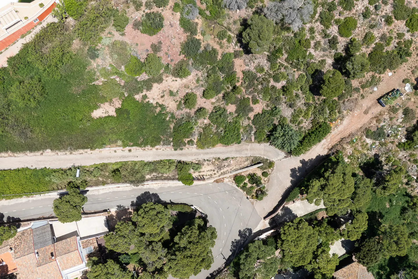 Aerial view of a property showing a road, a dirt path, green vegetation, and some buildings.