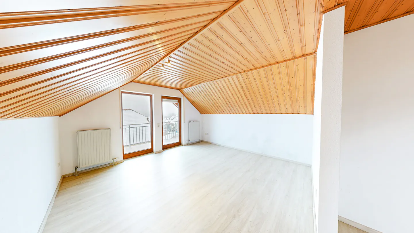 Empty attic room with light wood flooring, white walls, a sloped wood-paneled ceiling, and a balcony door.