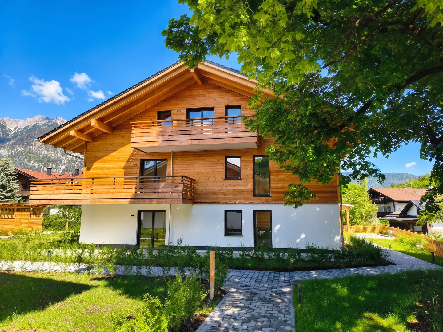 Two-story house with wood siding and a white foundation, set against a blue sky and mountain backdrop. A stone path leads to the house.