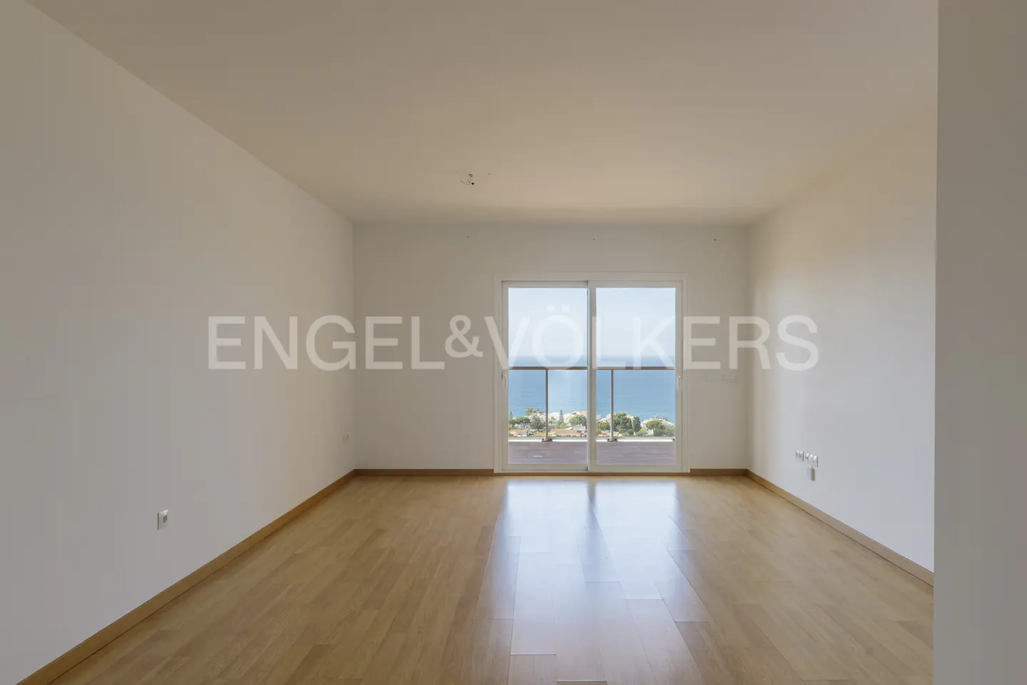 Empty room with light wood floors, white walls, and a sliding glass door opening to a balcony with a sea view.