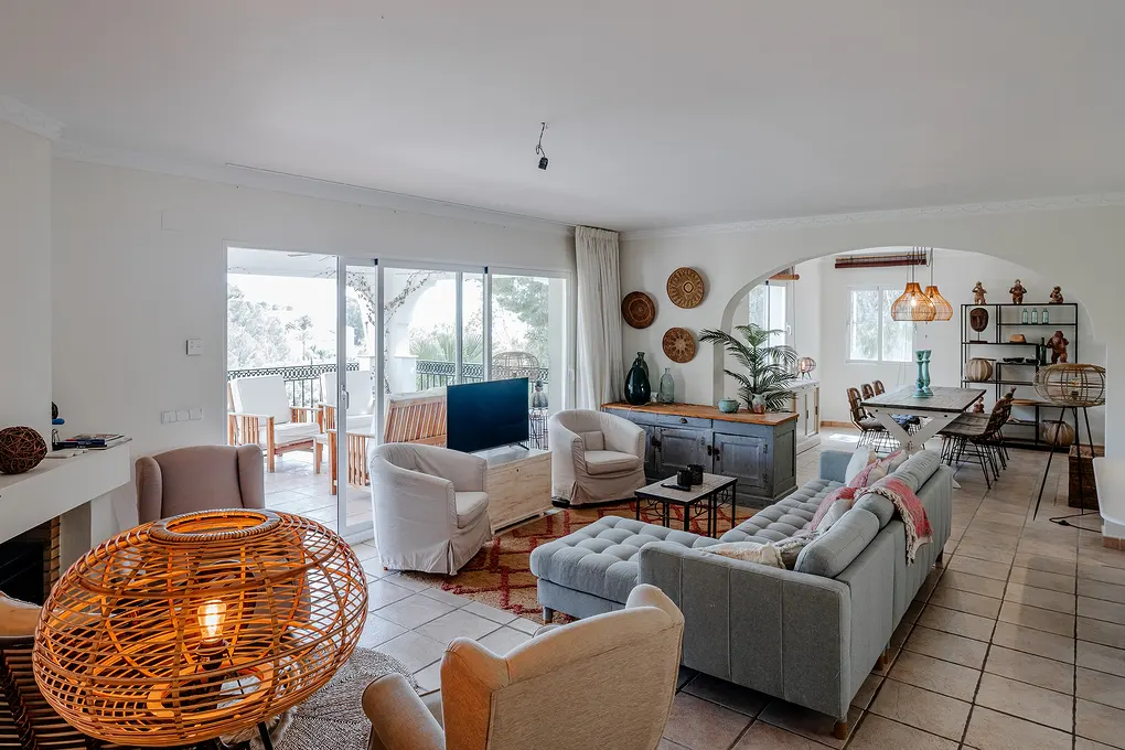 A bright living room with a gray sofa, white armchairs, and a dining area in the background. A large rattan lamp is in the foreground.