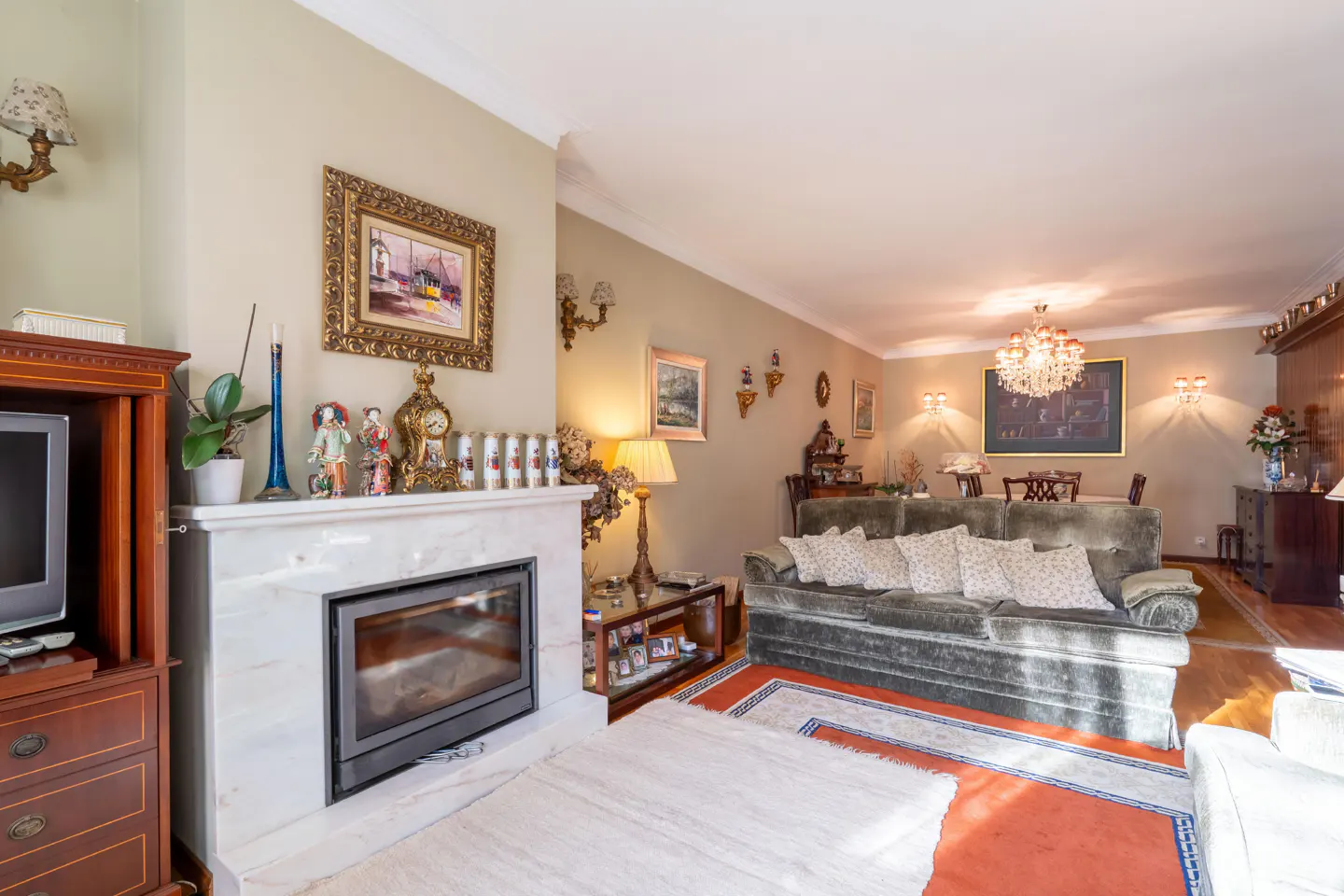 Living room with a marble fireplace, dark green sofa, and dining area with a chandelier.