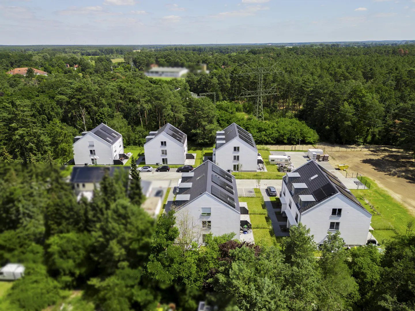 Aerial view of modern white houses with solar panels, surrounded by lush green trees and a blue sky.