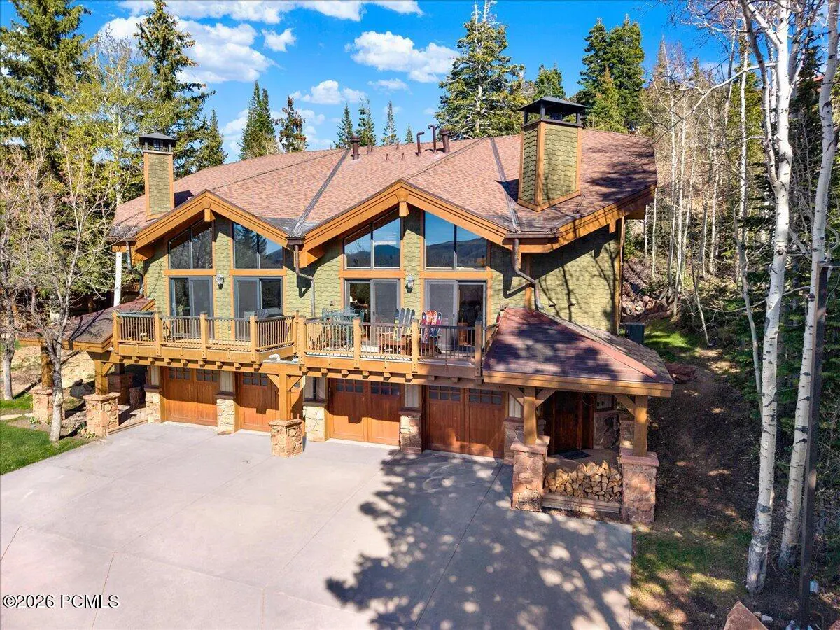 Exterior view of a large, green mountain home with brown trim, a brown roof, and a three-car garage. The home has balconies and is surrounded by trees.