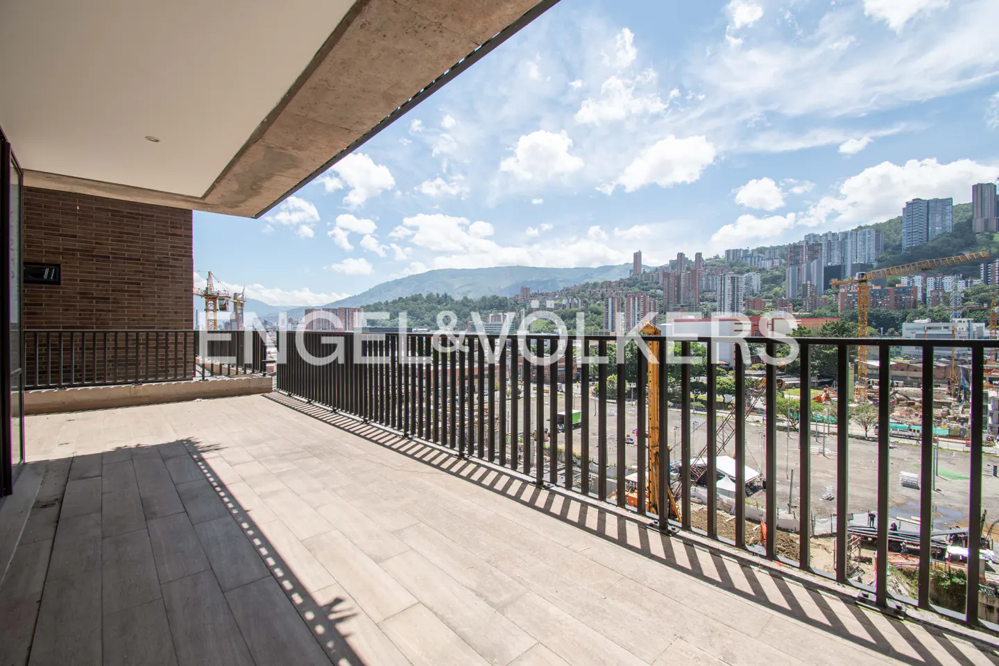 Balcony view with black railings overlooking a city skyline and mountains under a blue sky with clouds.
