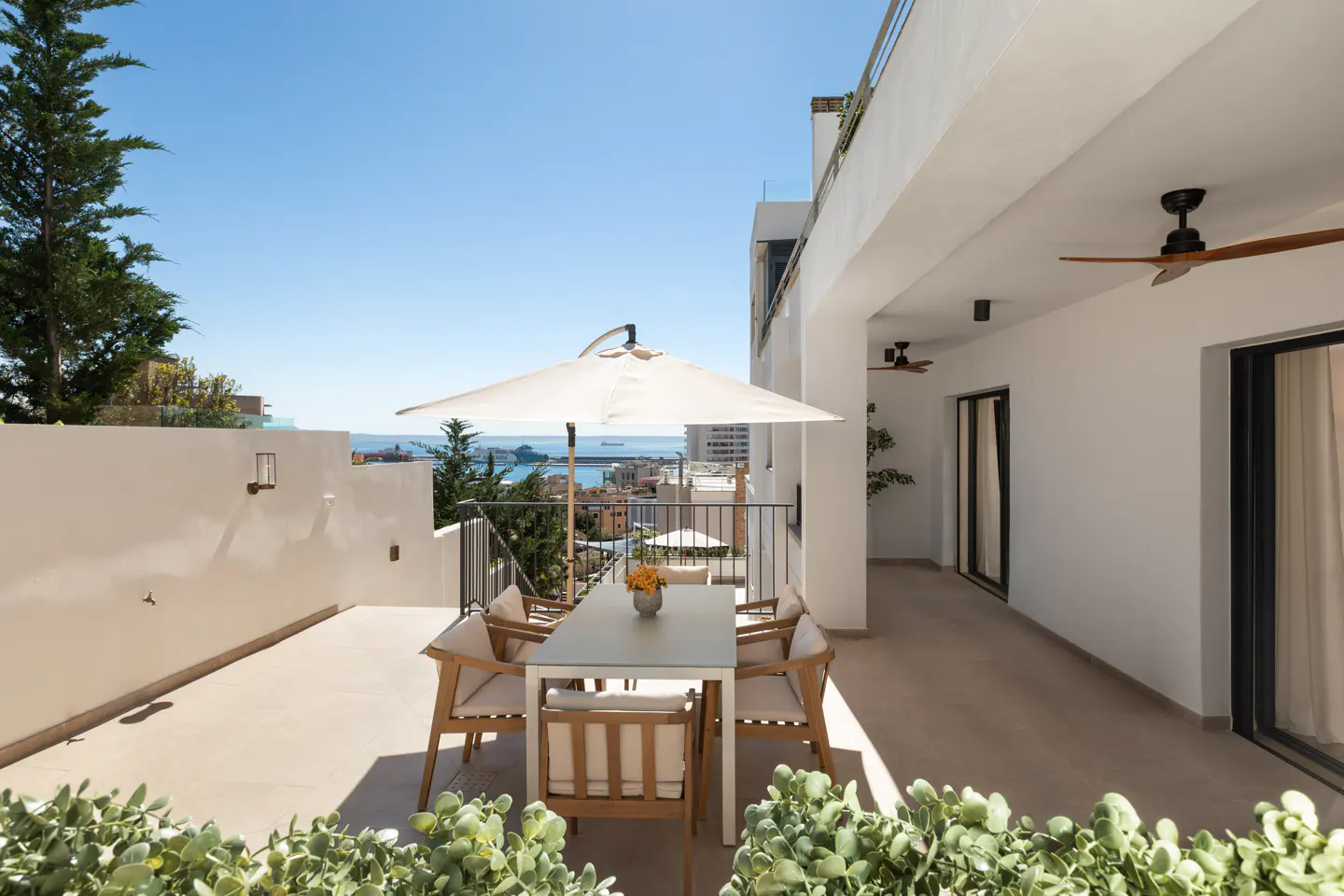Outdoor patio with a white table, chairs, and umbrella overlooking the ocean on a sunny day.