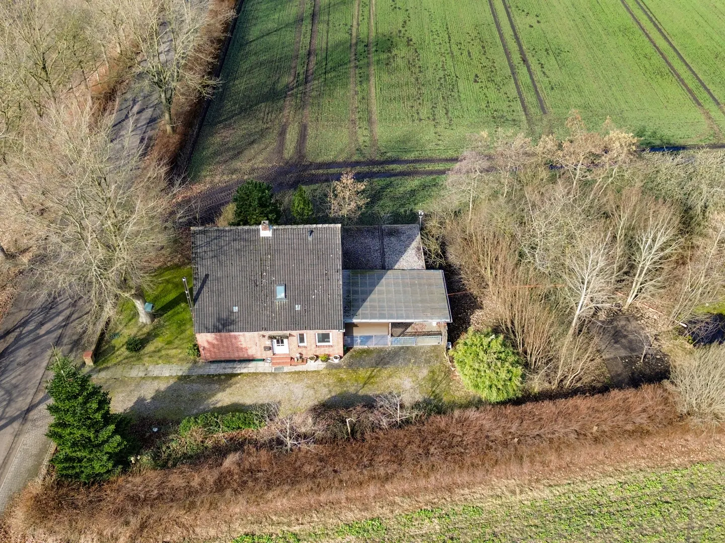 Aerial view of a red brick house with a gray roof, surrounded by green fields and trees.