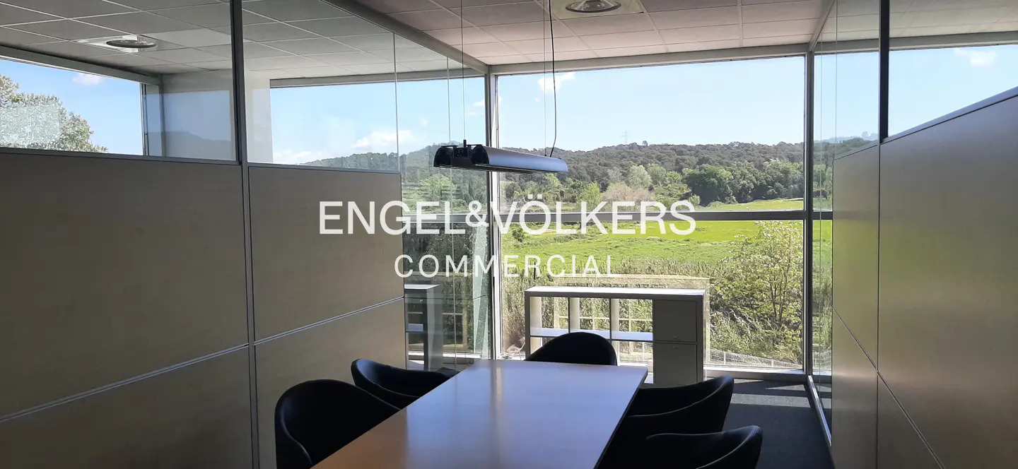 Office conference room with a long table, black chairs, and a window view of green fields and trees. "Engel & Volkers Commercial" logo on the glass.