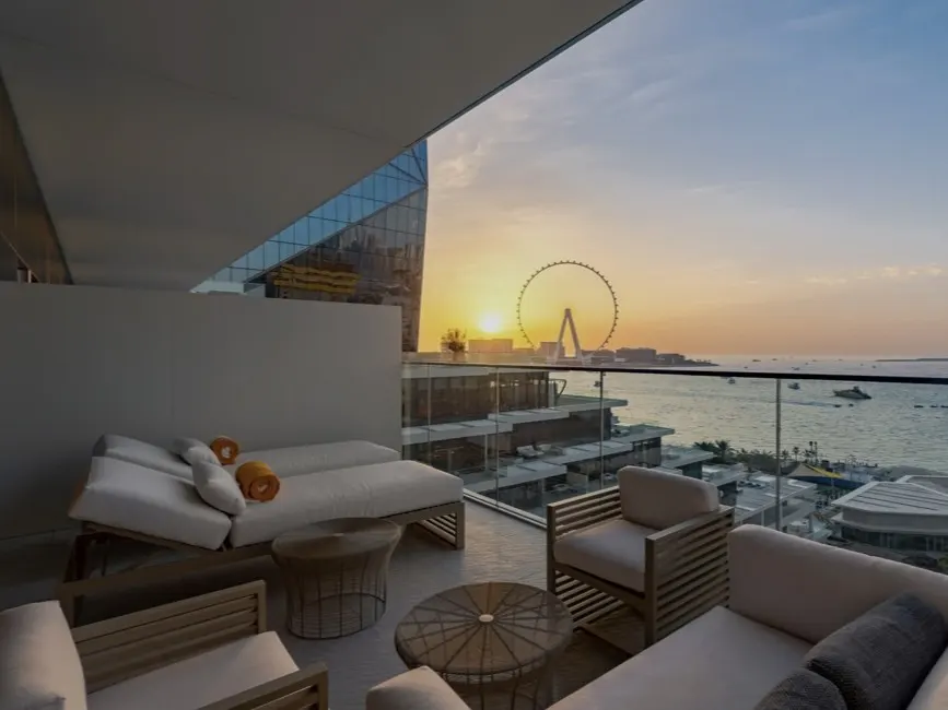 Balcony view at sunset. White lounge chairs and seating overlook the ocean and Ain Dubai Ferris wheel.