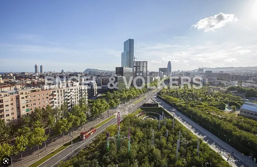 Barcelona cityscape view with modern buildings, green park, and a red tour bus on a sunny day. Engel & Volkers logo overlay.