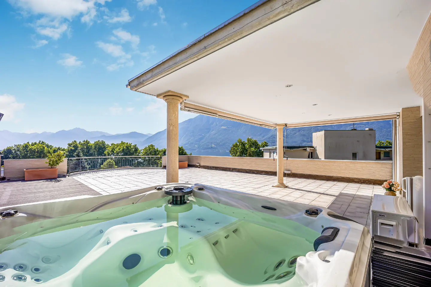 Outdoor patio with a hot tub, stone pillars, and mountain views under a blue sky.