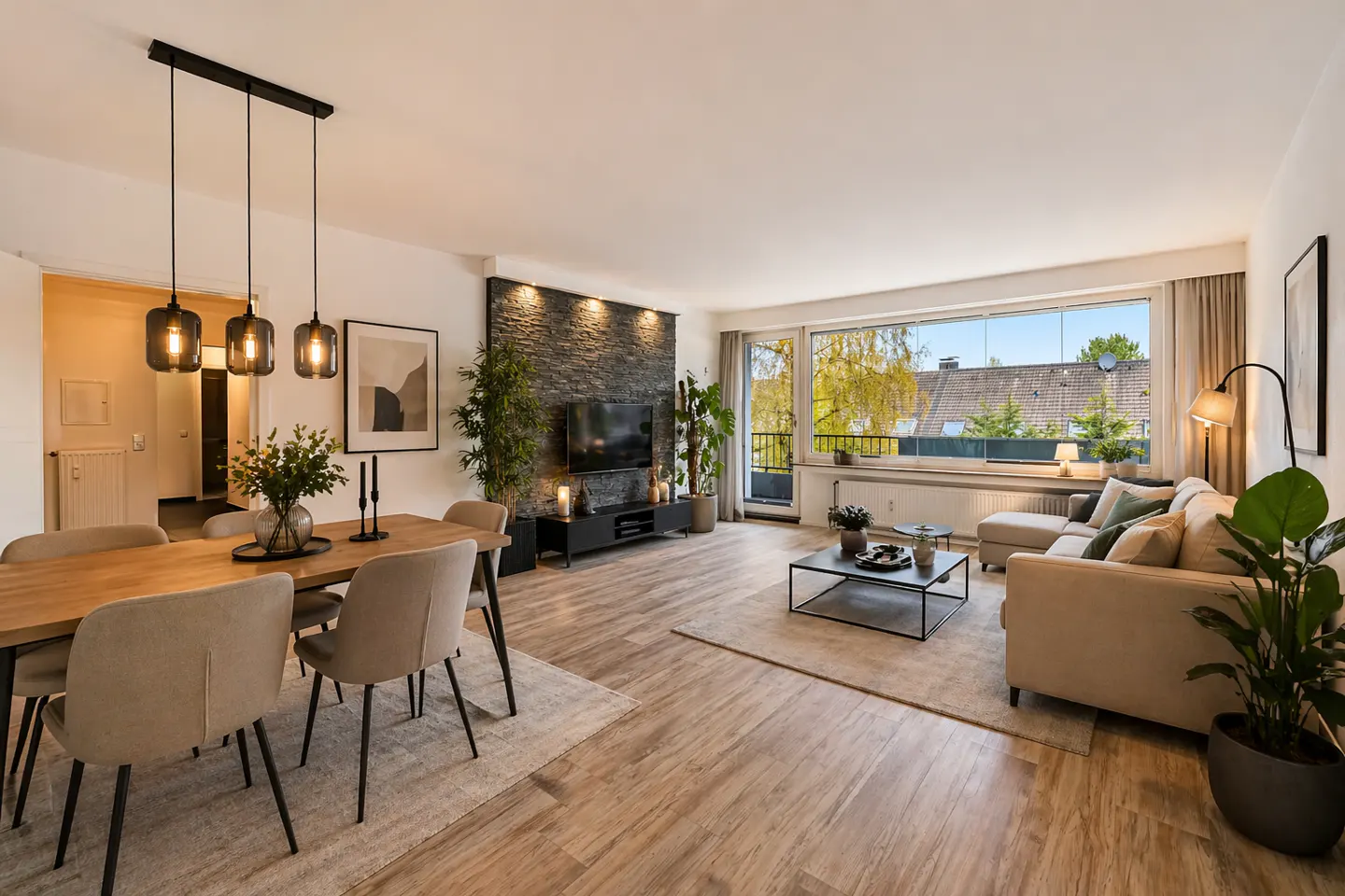 Bright living room with dining area. Wood table with six chairs, stone accent wall with TV, and large window with view.