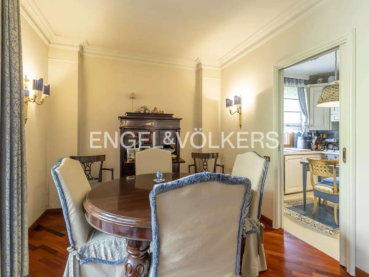 Dining room with a dark wood table and upholstered chairs. A dark wood cabinet is in the background. A doorway leads to a kitchen.