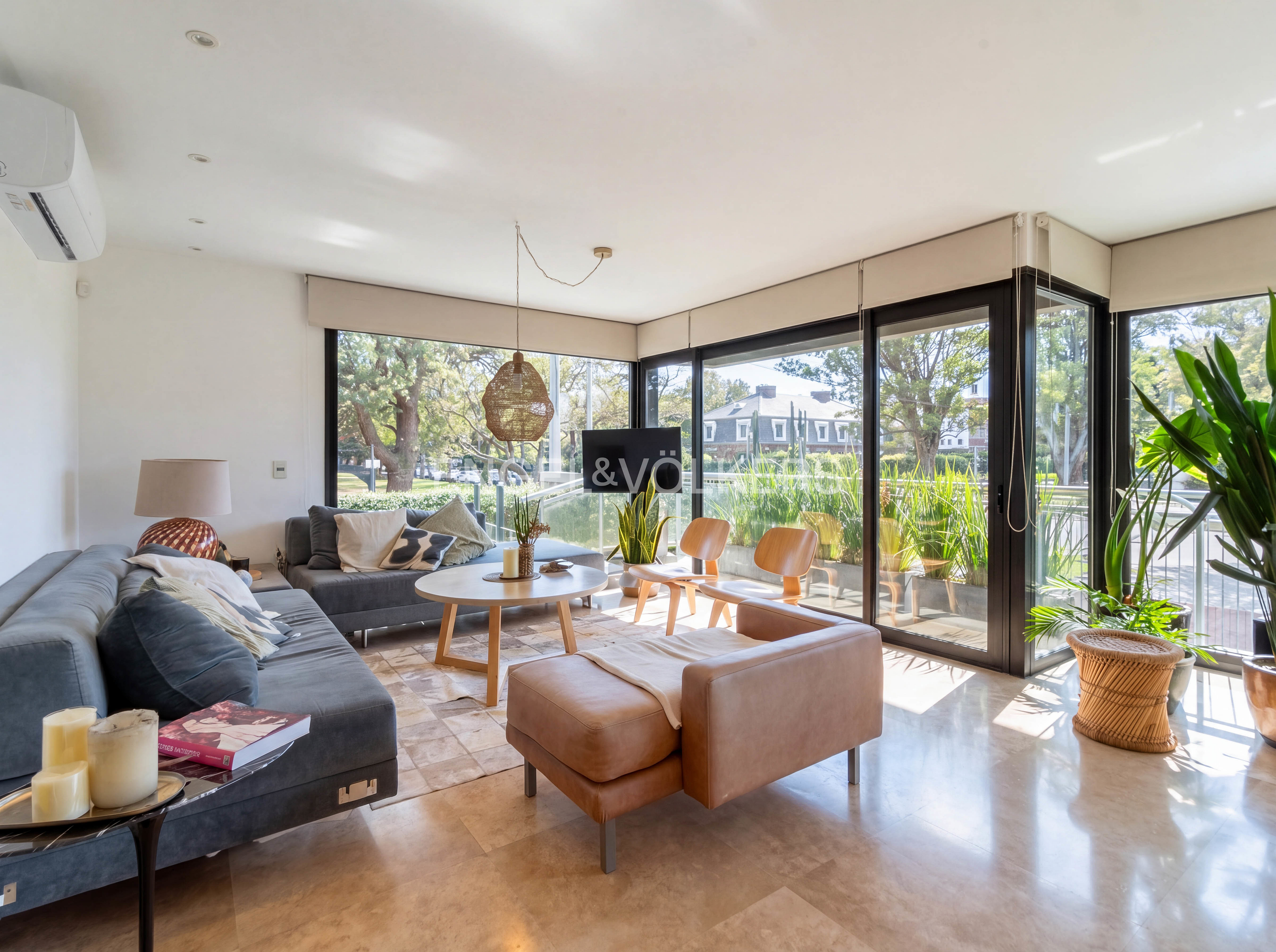 Bright living room with gray sofas, a brown leather chair, and large windows overlooking a green outdoor space.