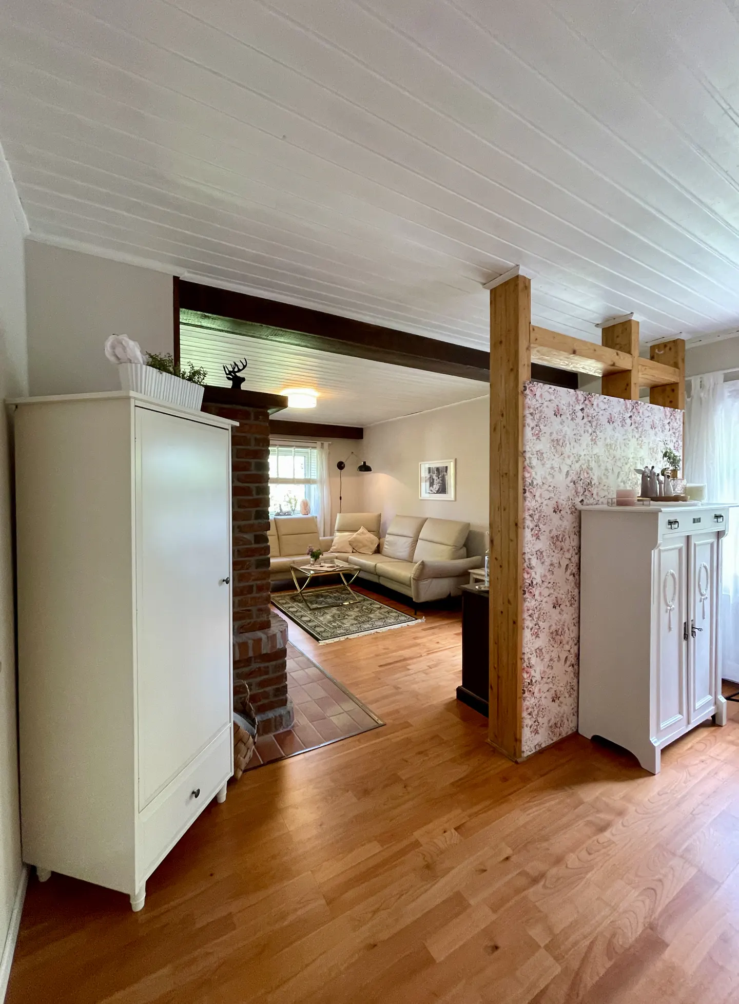 Open-concept living room with hardwood floors, white cabinets, and a brick fireplace. A beige sectional sofa is visible in the background.