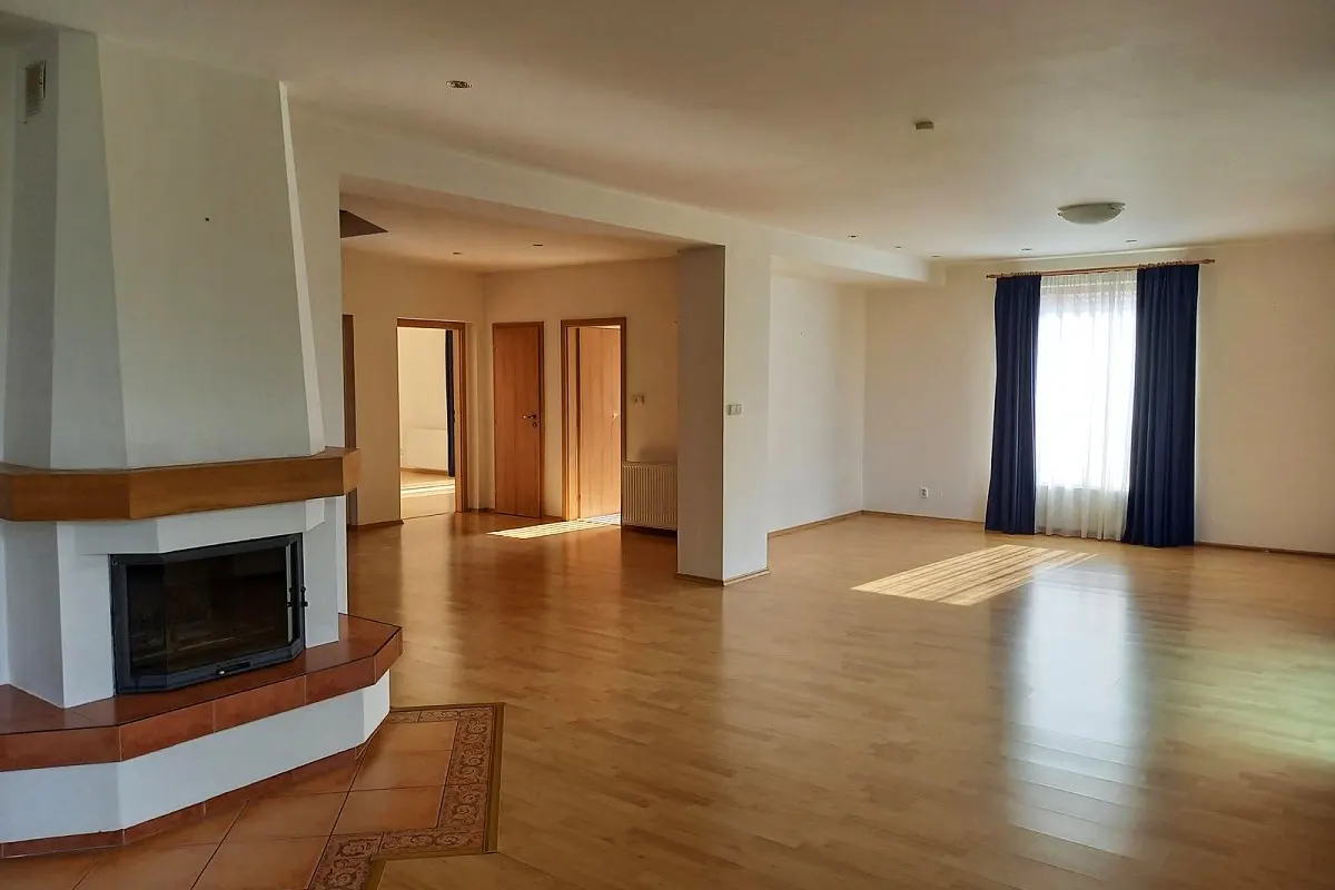 Bright, empty living room with hardwood floors, a fireplace, and blue curtains. Three doors are visible in the background.