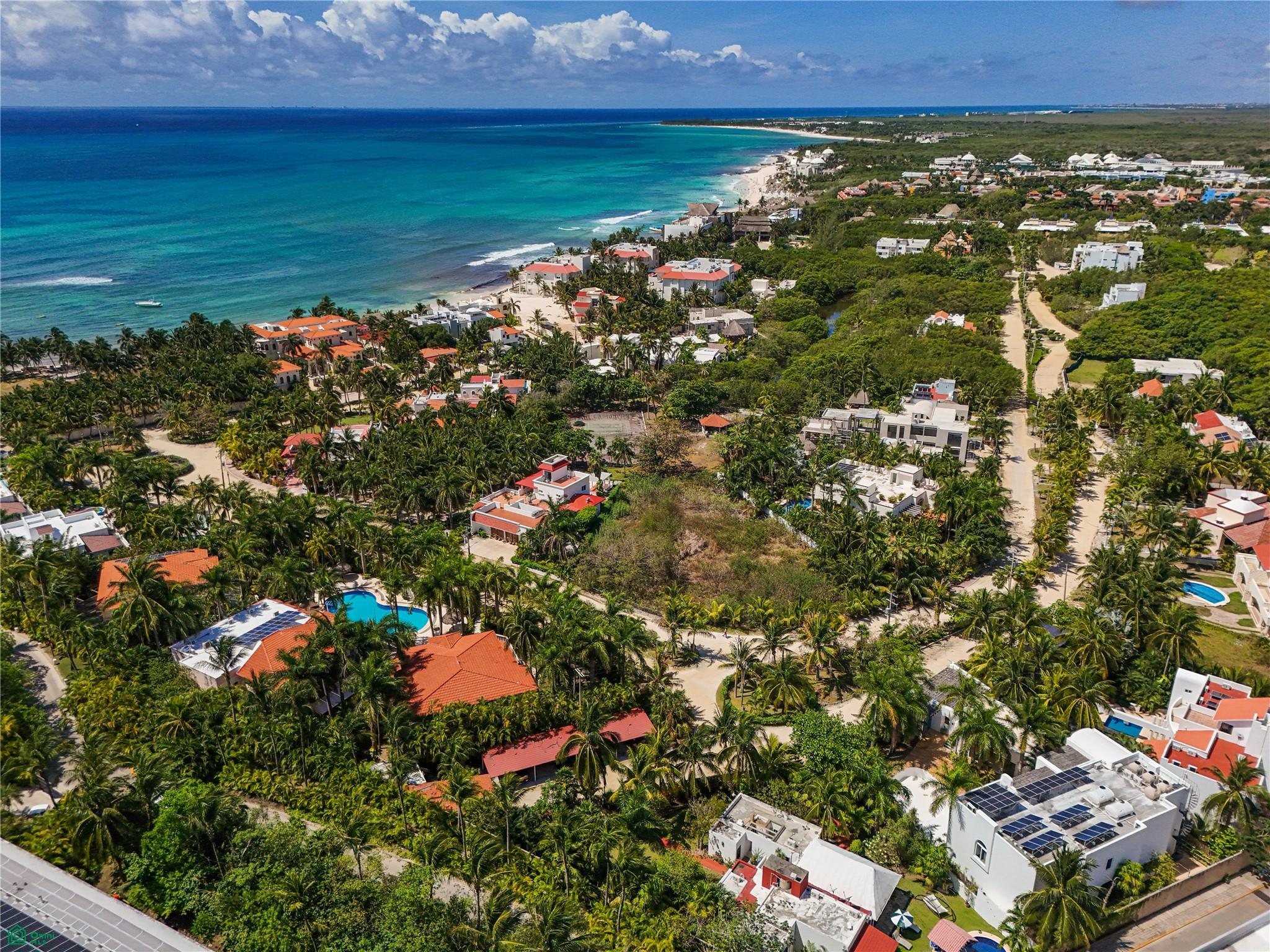 Aerial view of a tropical coastal community with lush greenery, red-roofed villas, swimming pools, and a turquoise ocean. [AI-generated text]