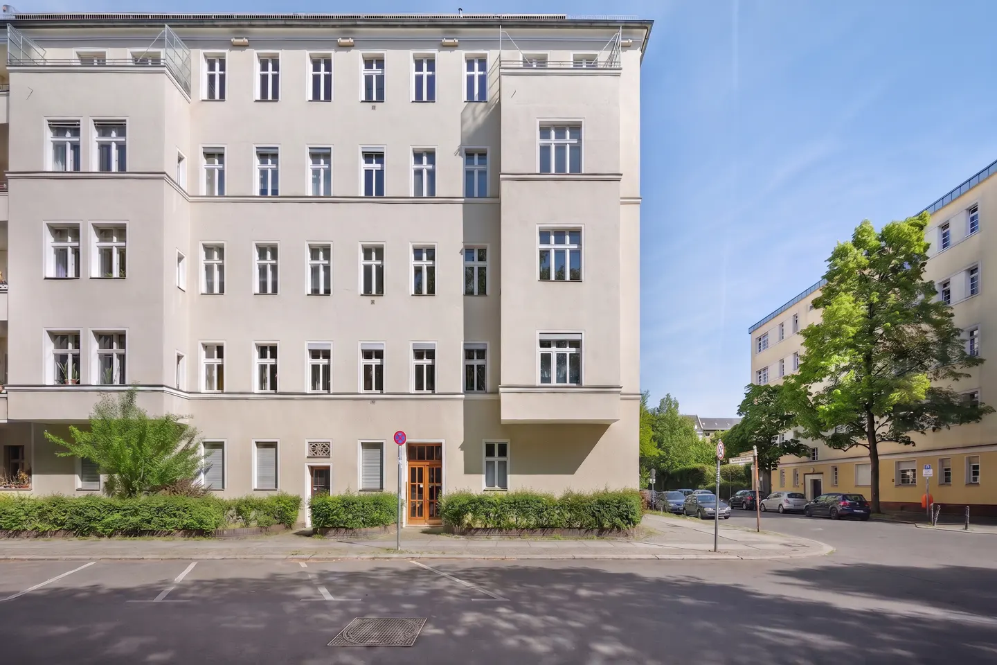 Exterior of a light beige apartment building with white framed windows and a brown door, street view.