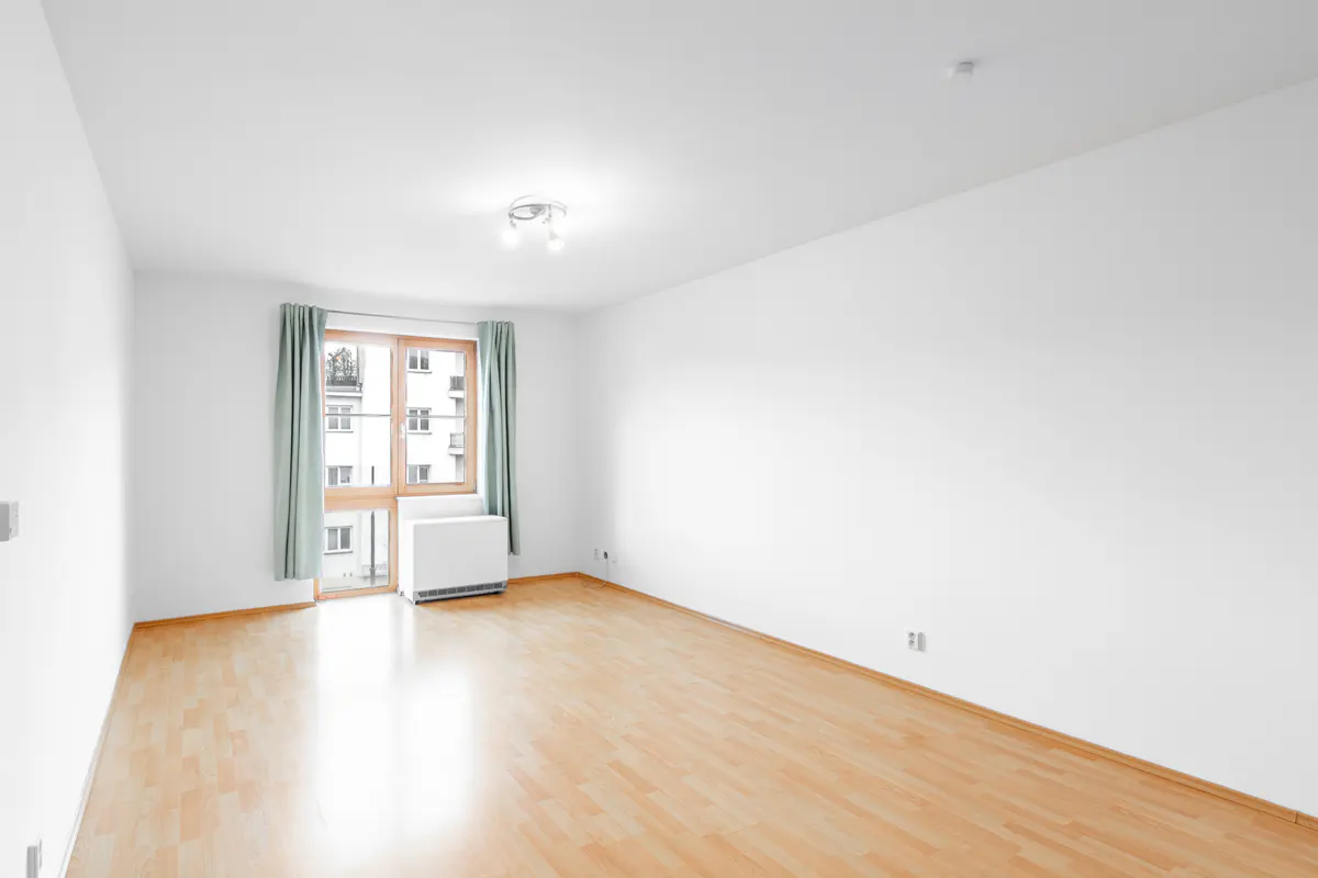 Empty room with white walls, light wood flooring, a window with sage curtains, and a white radiator.