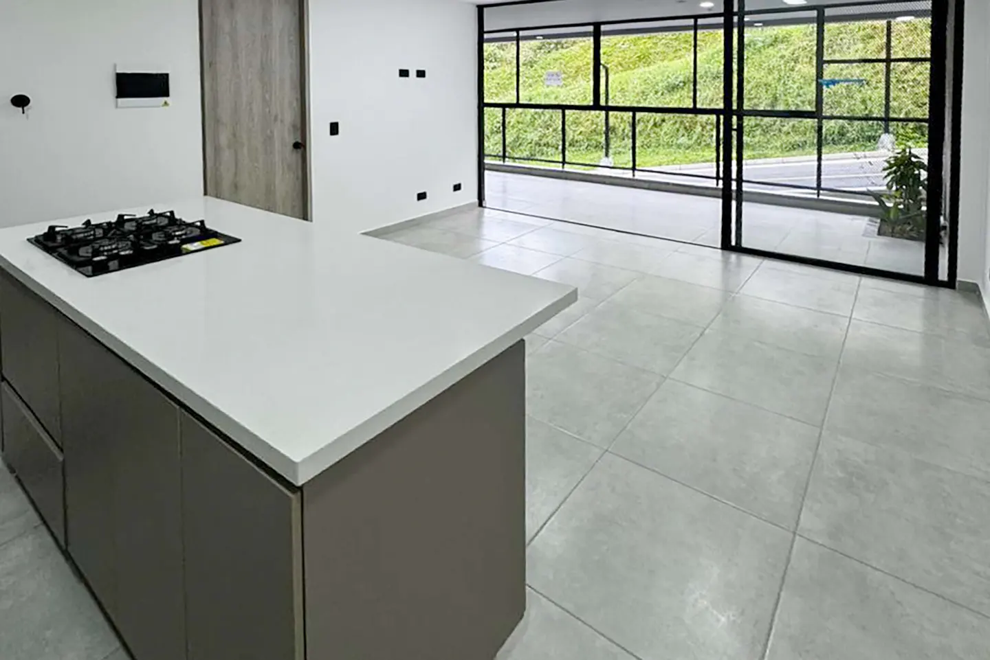 A modern kitchen with a white countertop island and a black gas stove. Large windows offer a view of green hills.