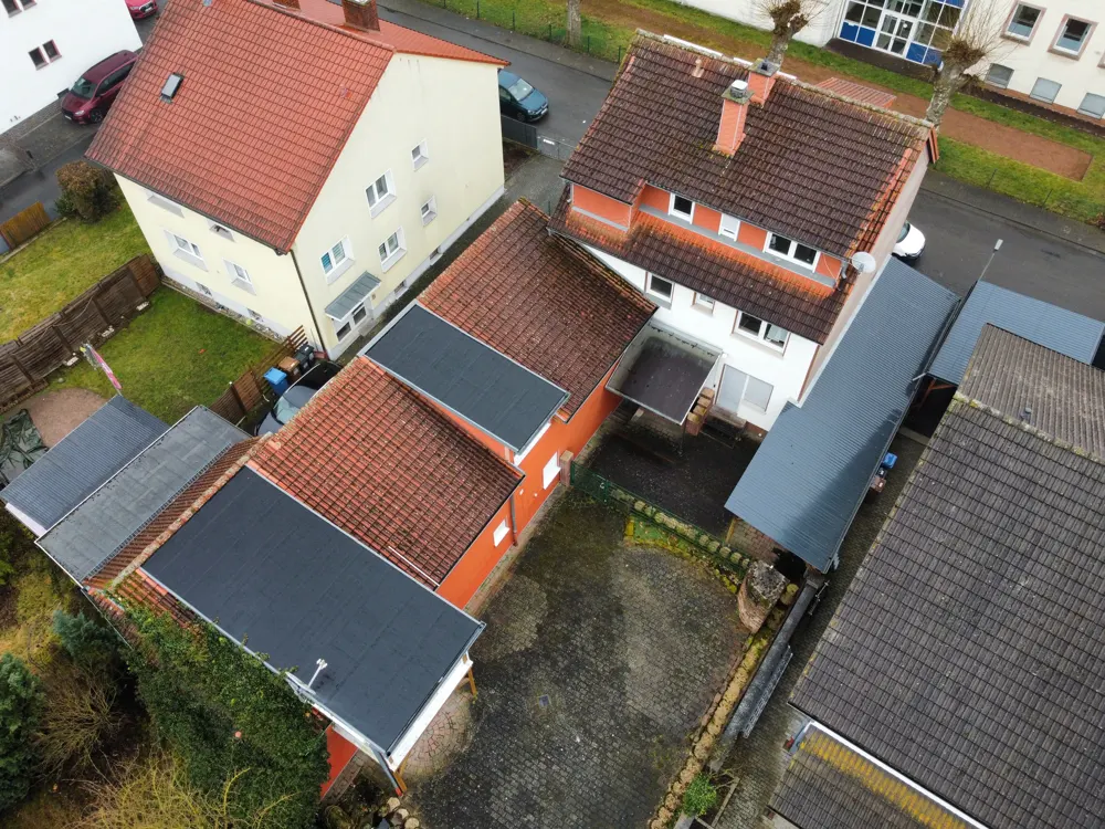 Aerial view of houses with red and gray roofs, green lawns, and paved courtyards.
