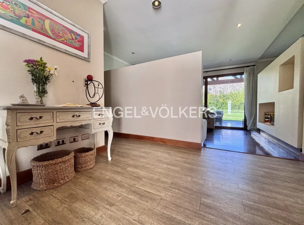Entryway with wood-look tile floor, a white desk with flowers, and Engel & Völkers logo on the wall. A living room is visible through a doorway.