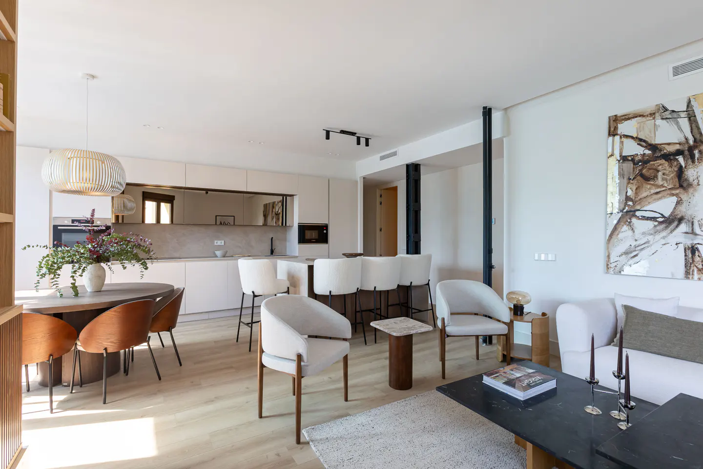Open-concept living space with a kitchen, dining area, and living room. White walls, light wood floors, and modern furniture.