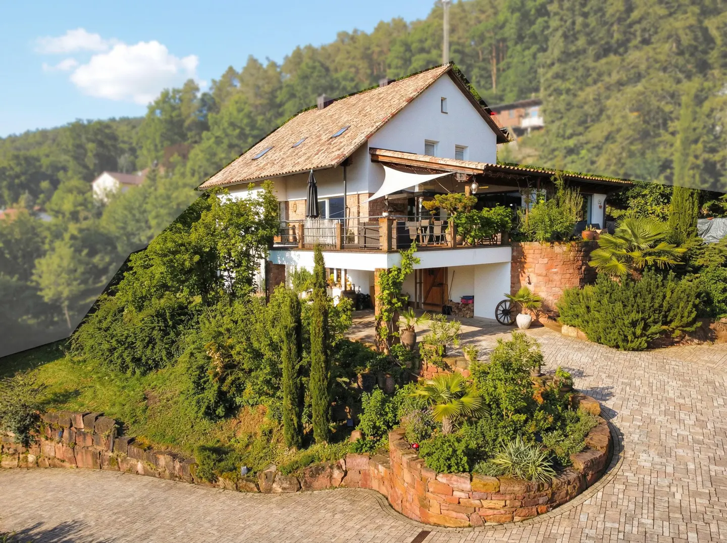 A two-story white house with a brown tile roof, a large deck, and lush green landscaping on a sunny day.