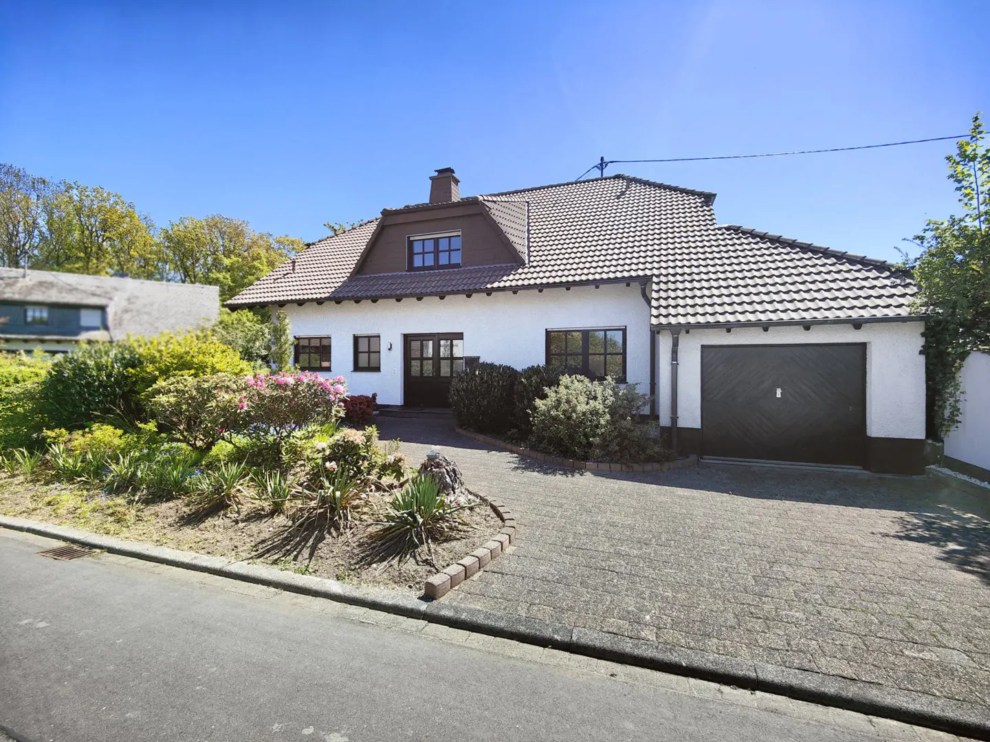 Front exterior of a white house with a brown roof and a black garage door. A garden is in front.