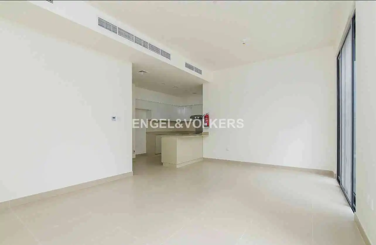 An empty, bright room with white walls and tile floors. A kitchen area is visible in the background. Engel & Völkers logo is displayed.
