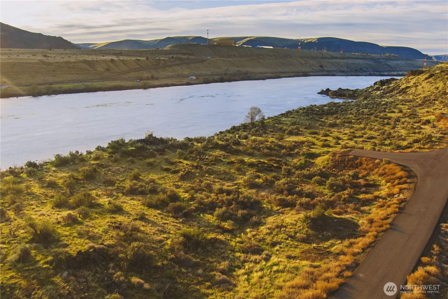 Scenic view of a wide river flowing through a hilly landscape with green and brown vegetation and a road.