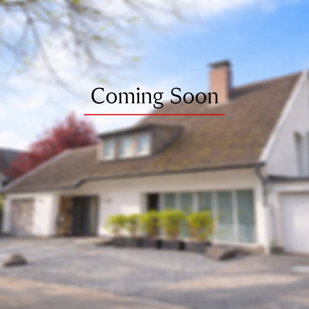 Blurred image of a white house with a brown roof and the text "Coming Soon" in black with a red line underneath.