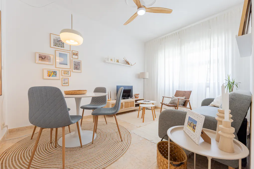 Bright living room with a dining area, grey chairs, round rug, sofa, and modern decor in a light, neutral color palette.