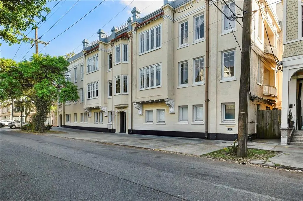 Street view of a cream-colored, multi-story apartment building with white-framed windows and decorative architectural details.