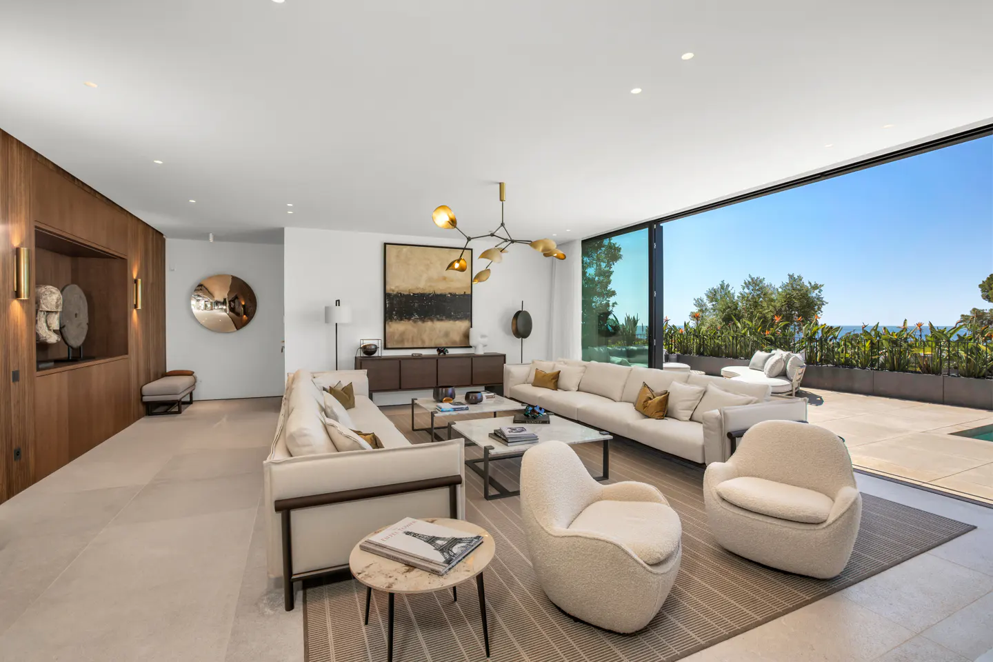Bright, modern living room with white sofas, chairs, and a large sliding glass door to a patio with ocean views.