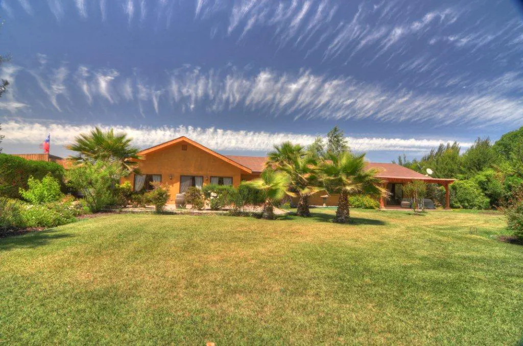 A single-story, orange house with a brown roof, palm trees, and a green lawn under a blue sky with streaky clouds.
