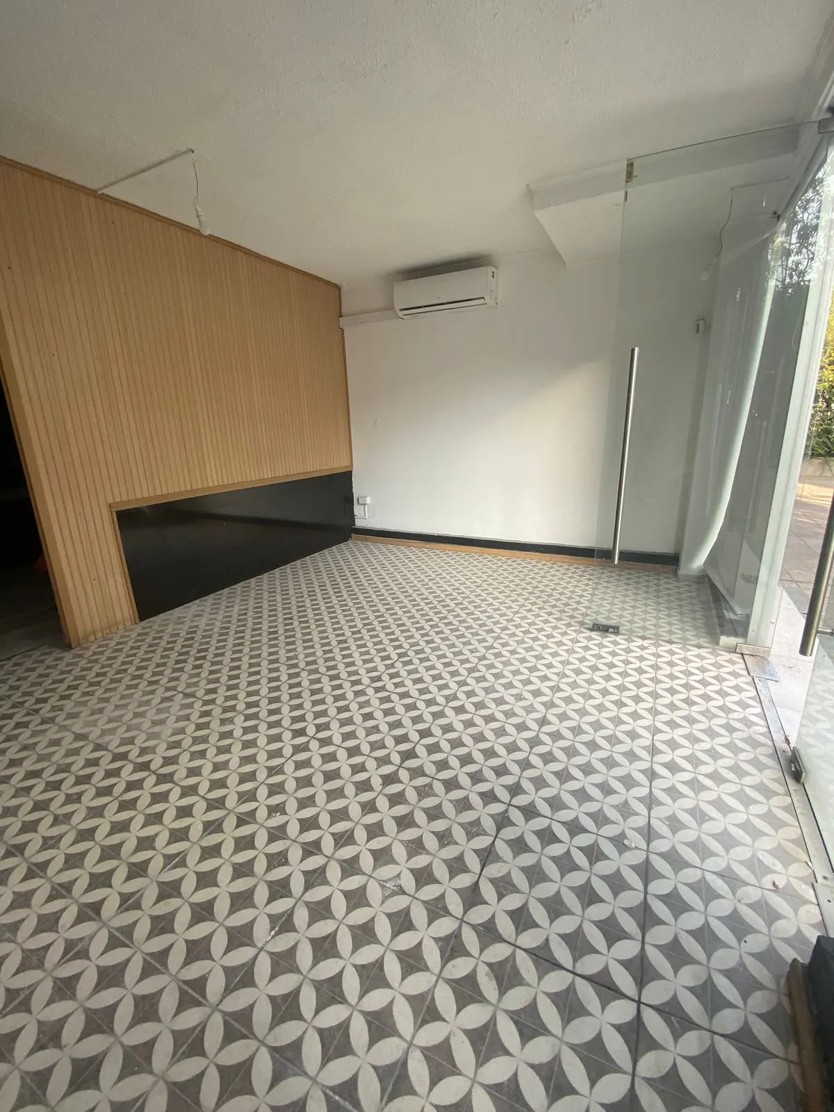 Empty commercial space with patterned tile floor, light wood accent wall, and glass storefront.