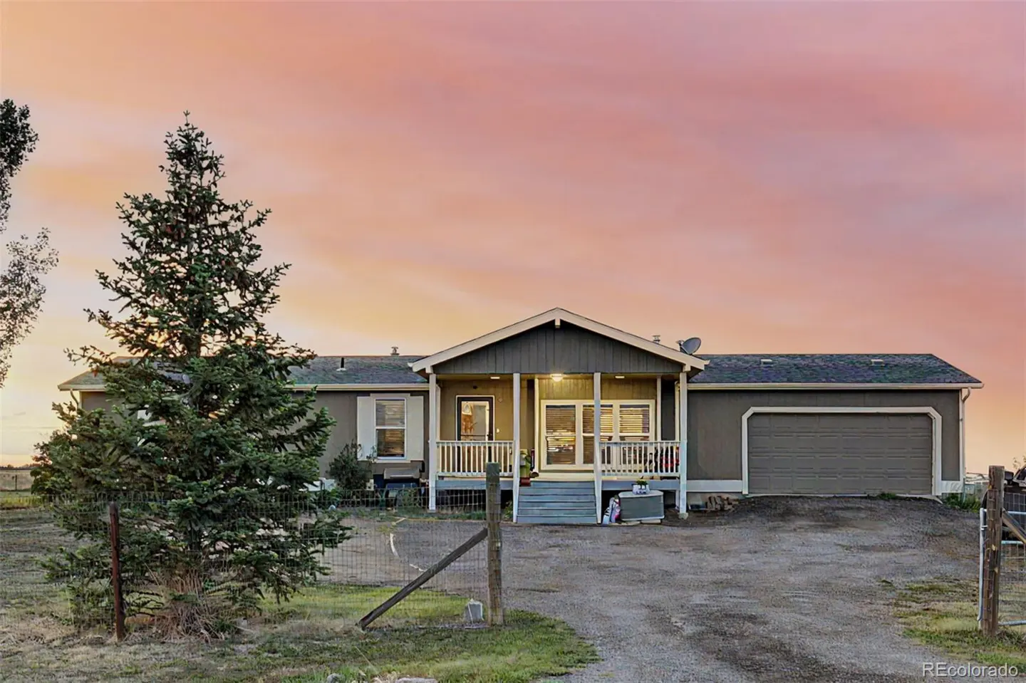 Single-story gray home with a front porch and attached garage under a vibrant pink and orange sunset sky.