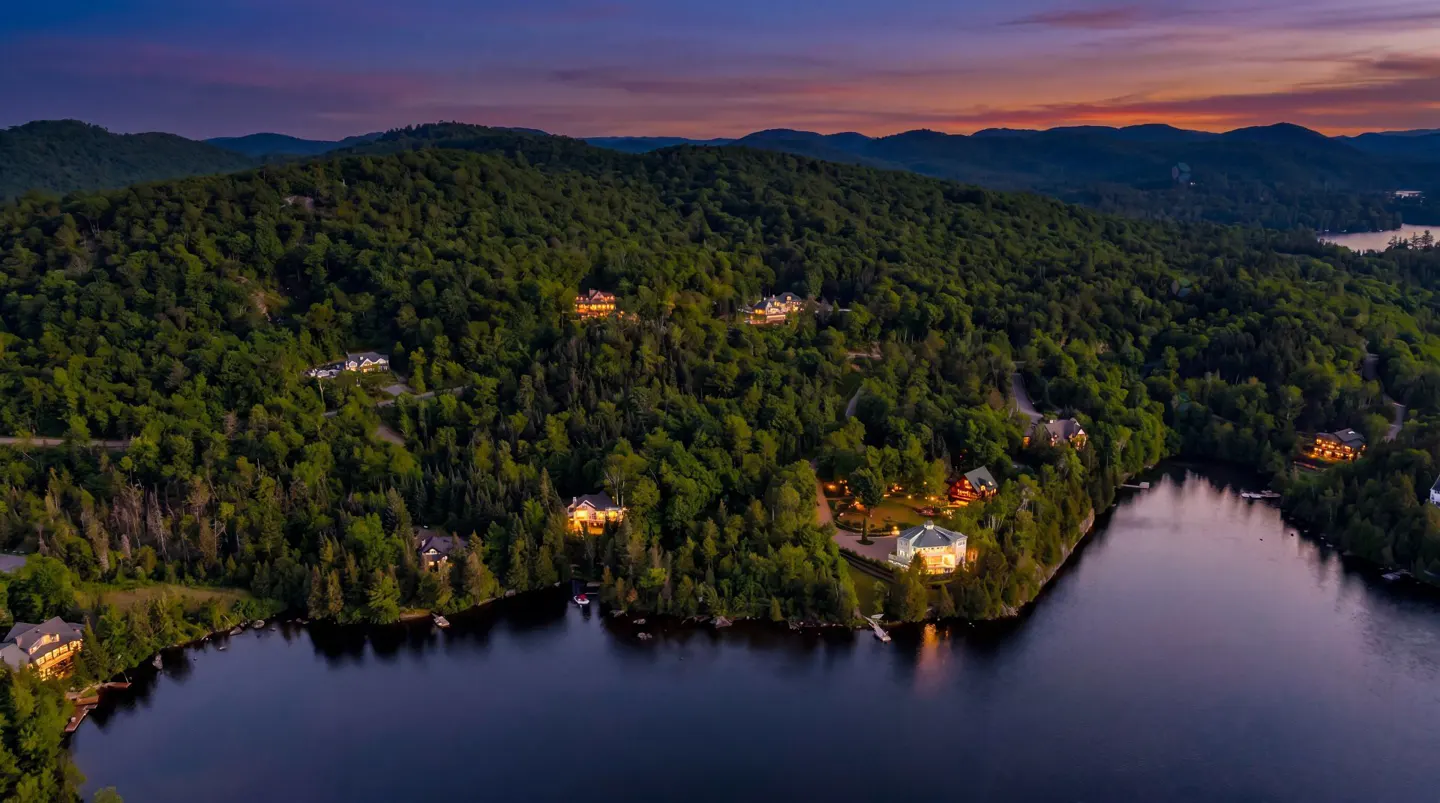Aerial view of luxury homes nestled in lush green hills surrounding a dark blue lake at dusk.