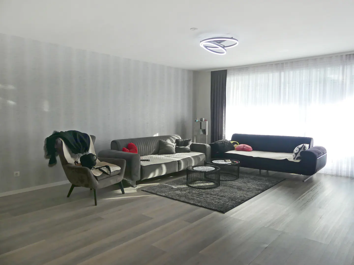 Living room with gray walls, light wood floors, and two sofas. A gray armchair sits to the left. Two round tables sit on a gray rug.