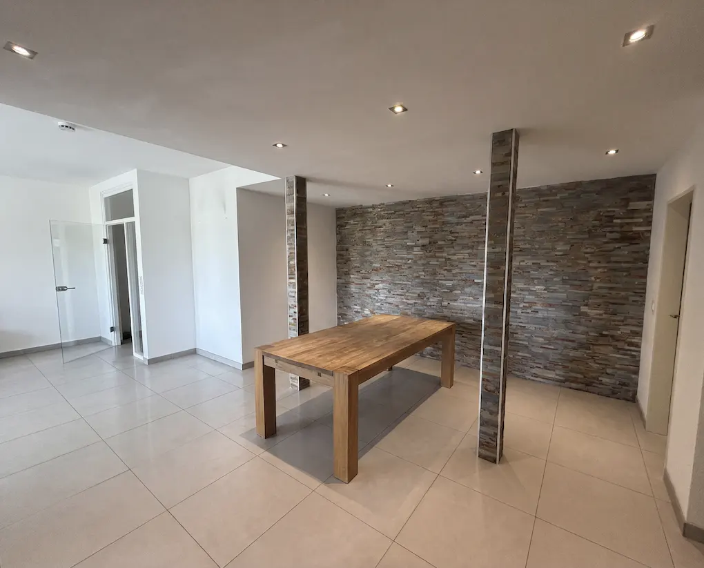 A bright, empty room with tile floors, a wood table, and a stone accent wall.