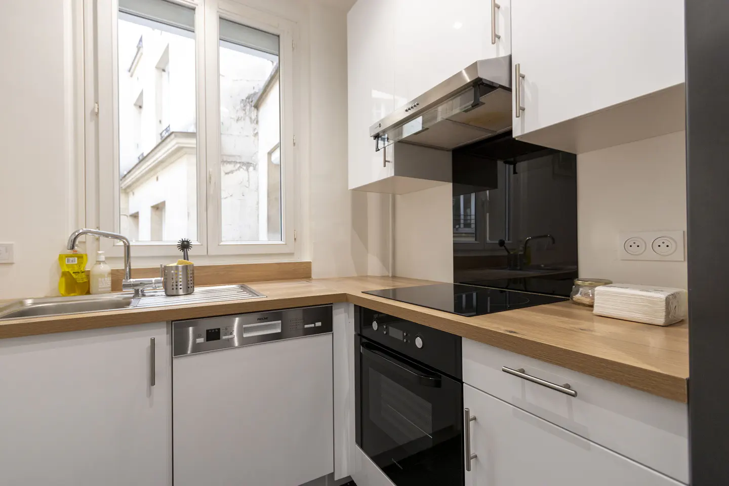 Bright kitchen with white cabinets, wood countertops, and stainless steel appliances. A window overlooks a building exterior.