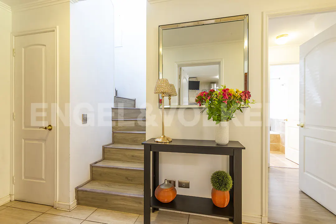 Entryway with wood-look stairs, a black console table featuring a lamp, colorful flowers, and decorative pots.