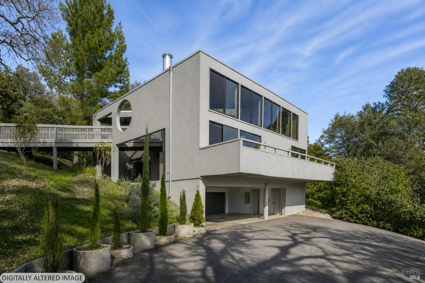 Exterior of a modern gray house with a round window and a wooden bridge.