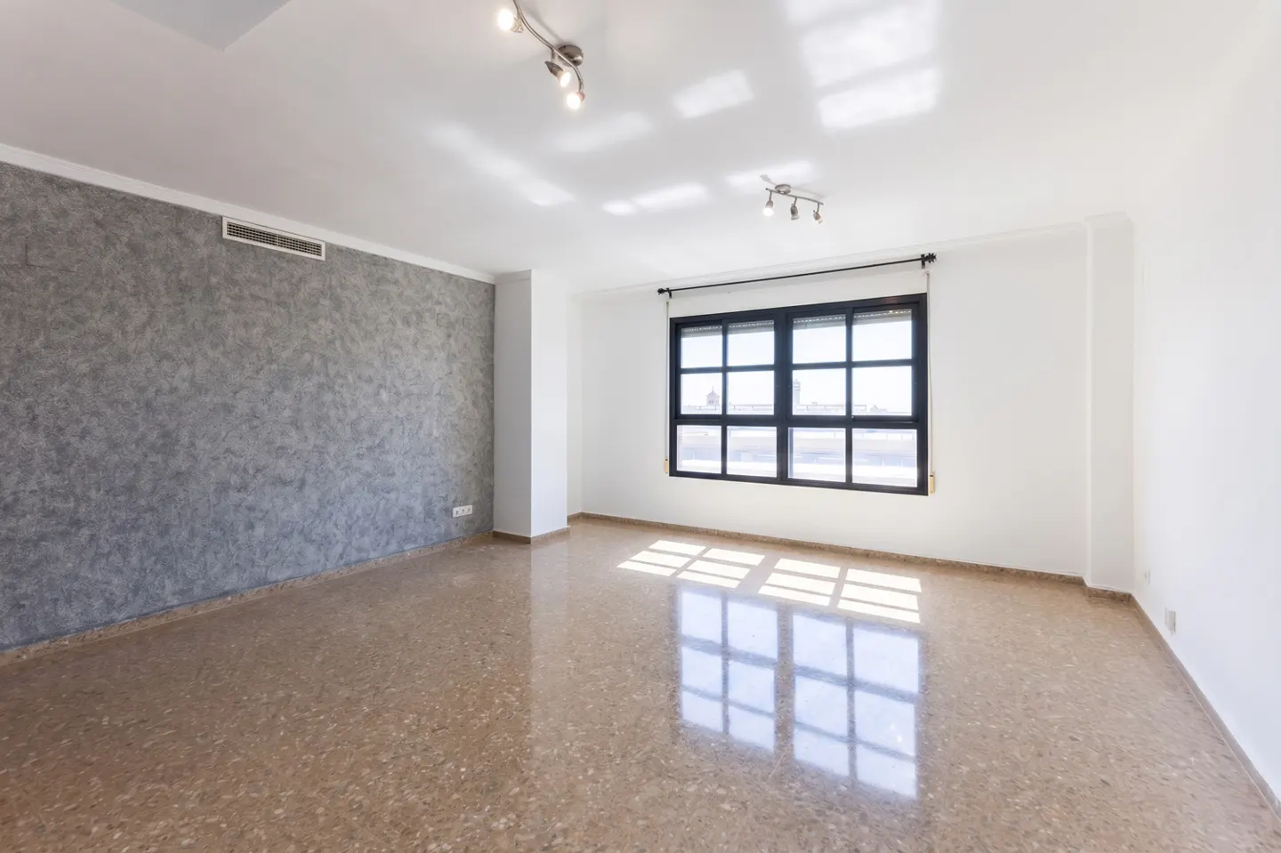 Empty room with white walls, a textured grey accent wall, polished stone flooring, and a large black-framed window.