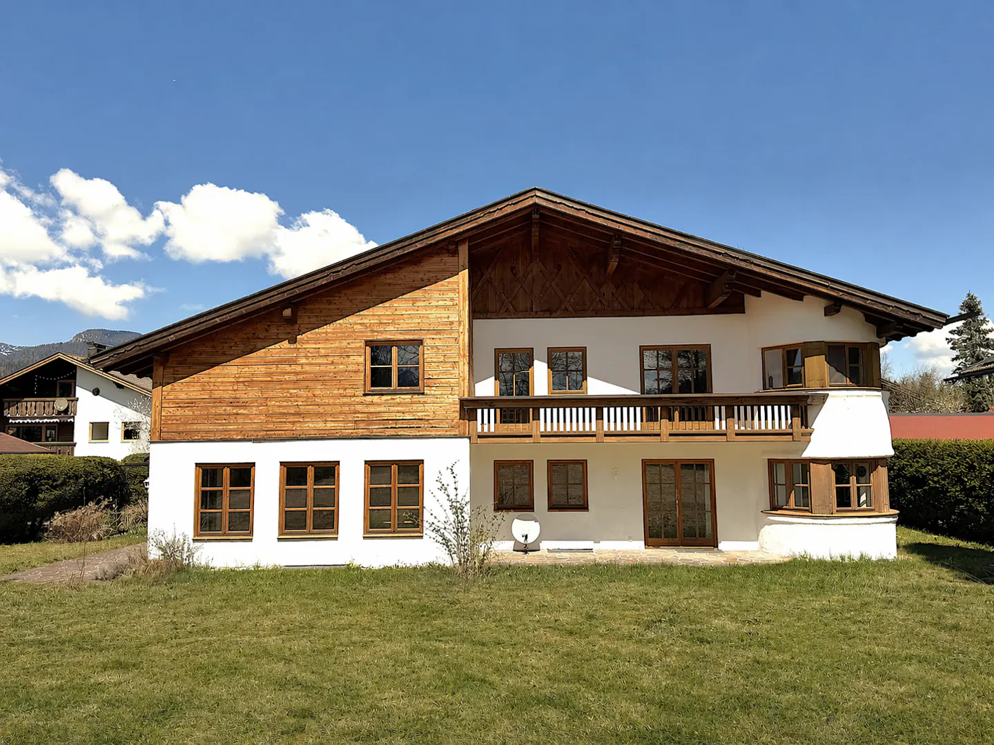 Two-story house with wood and white siding, brown trim, balcony, and green lawn under a blue sky.