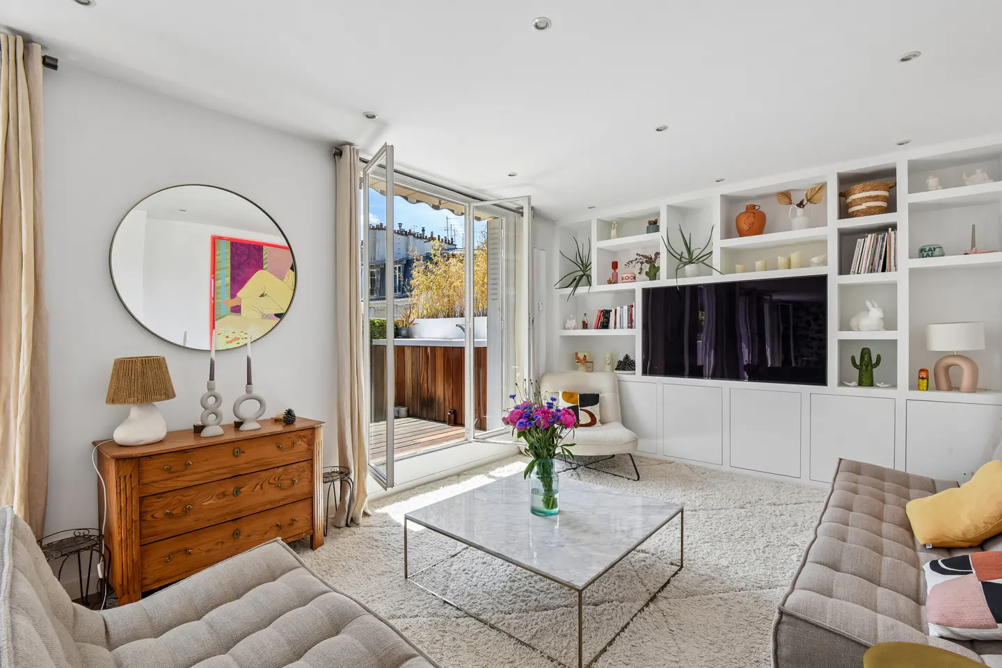 Bright living room with a wooden dresser, marble coffee table, white built-in shelving, and a balcony door.